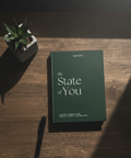 Guidet journal "The State of You" fra Superstate, designet for helse, klarhet og balanse, plassert på et trebord med en plante og penn.