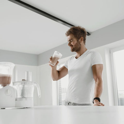 Mann som nyter en proteinshake i et moderne kjøkken, som fremhever fordelene med kollagenprotein for trening og helse.