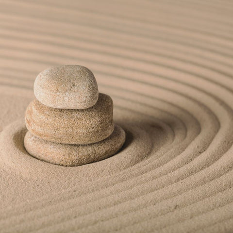 Tre stablede steiner i harmoni på sand med sirkelmønstre, som symboliserer ro, balanse og dyp søvn med Töff soppekstrakt.